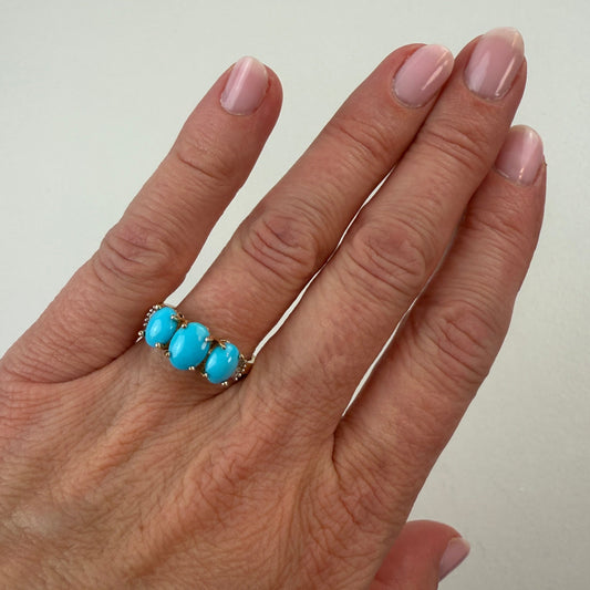 Hand wearing a ring with turquoise stones on a plain background