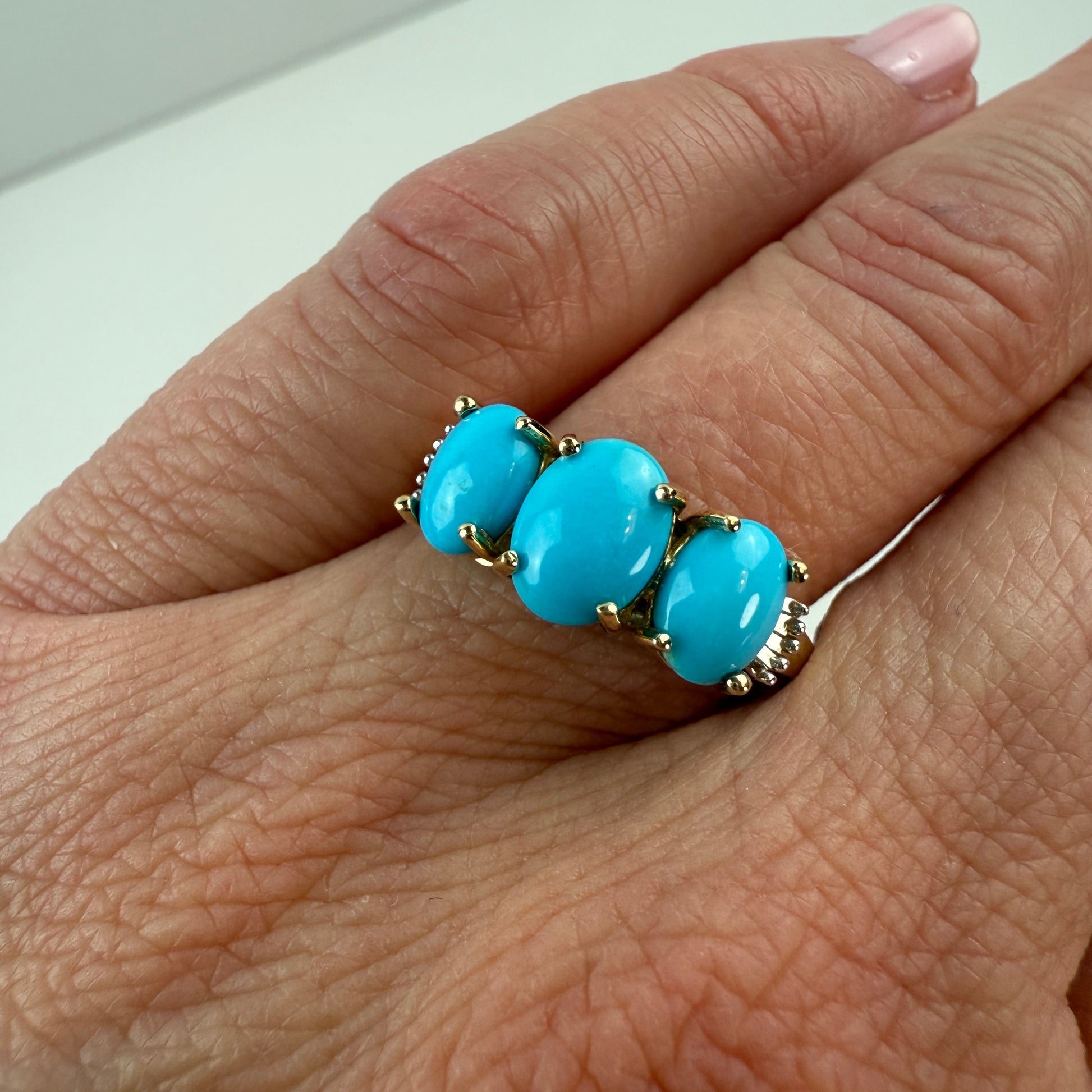 Turquoise ring with gold setting on a person's finger against a white background