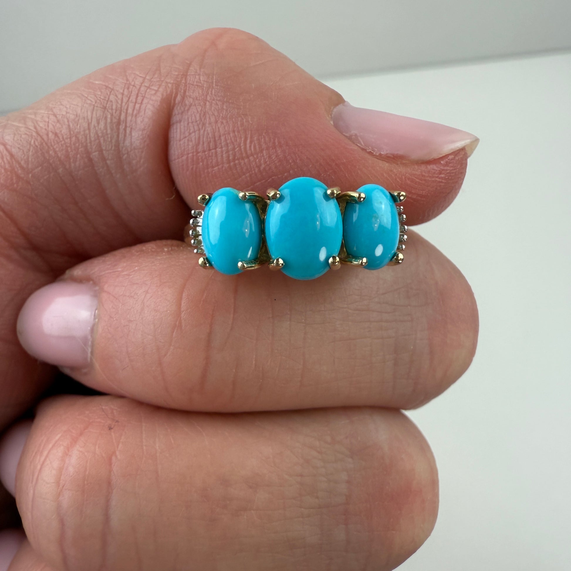 Turquoise ring with gold accents on a finger against a neutral background