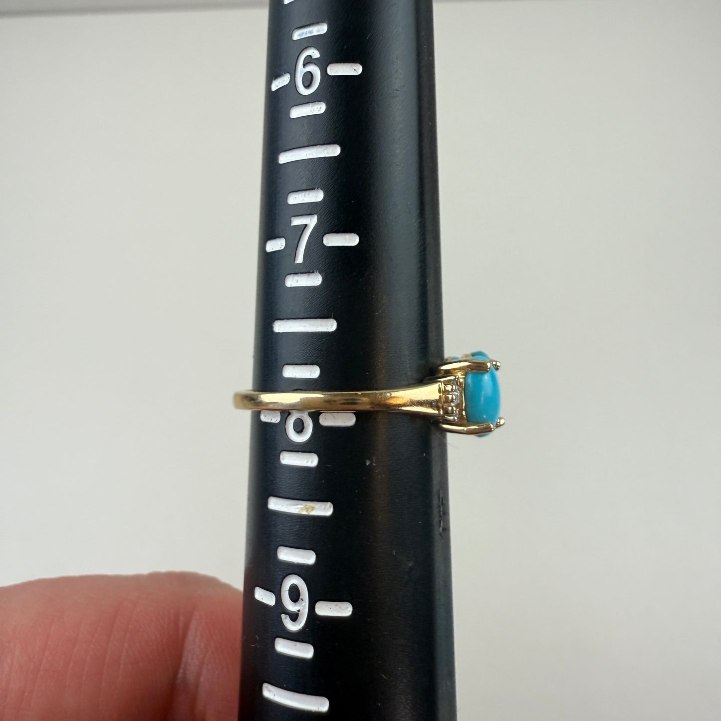 Gold ring with a blue turquoise on a black mandrel for size measurement, sits just above the 8.