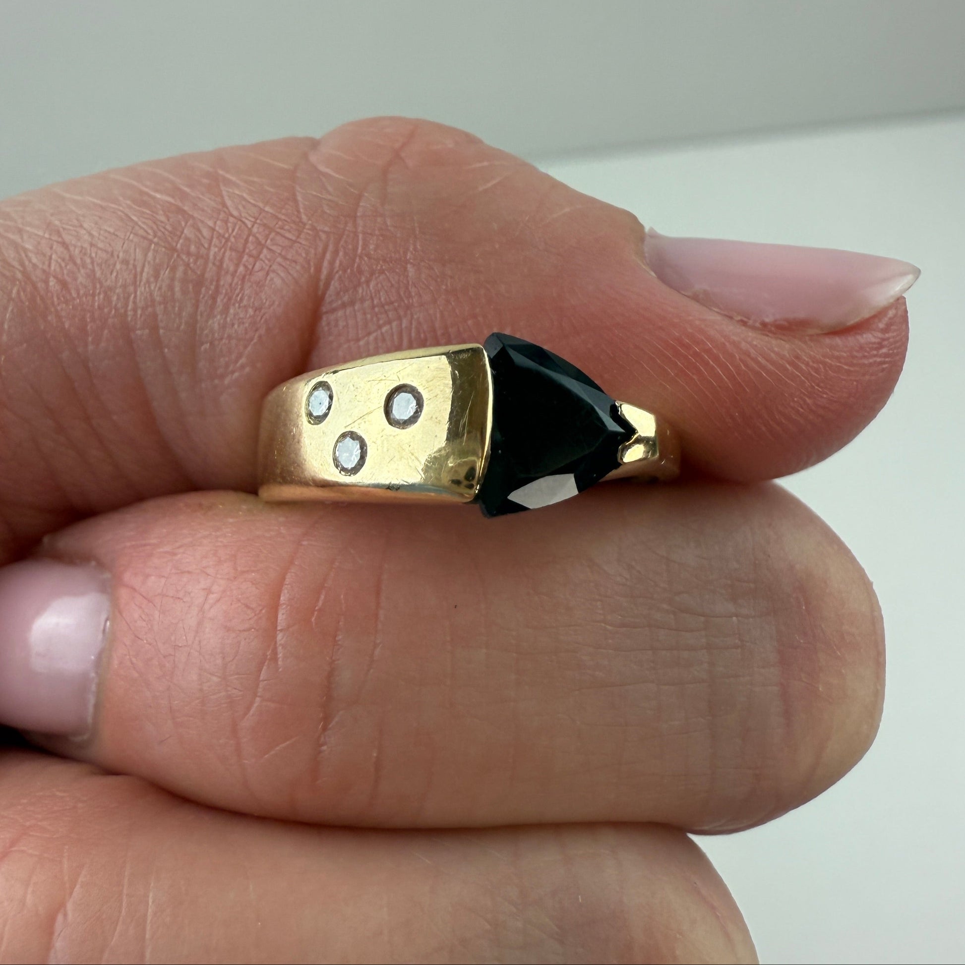 Gold ring with a black onyx between two fingers with a neutral background