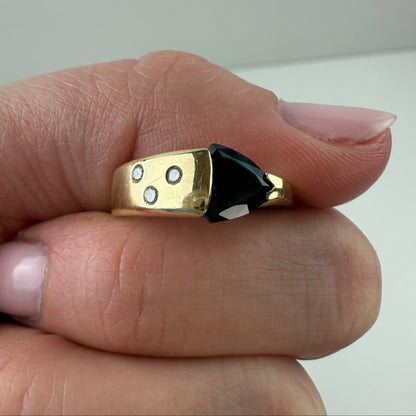 Gold ring with a black onyx between two fingers with a neutral background