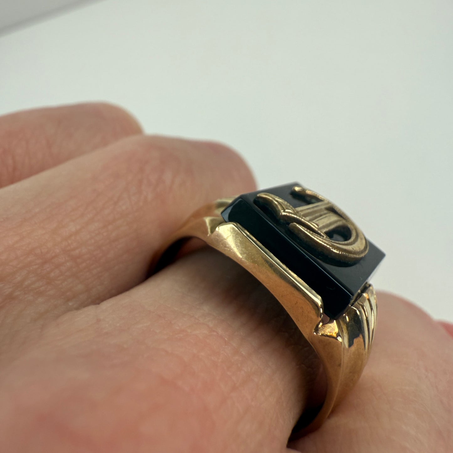 Gold ring with a black center on a finger against a white background