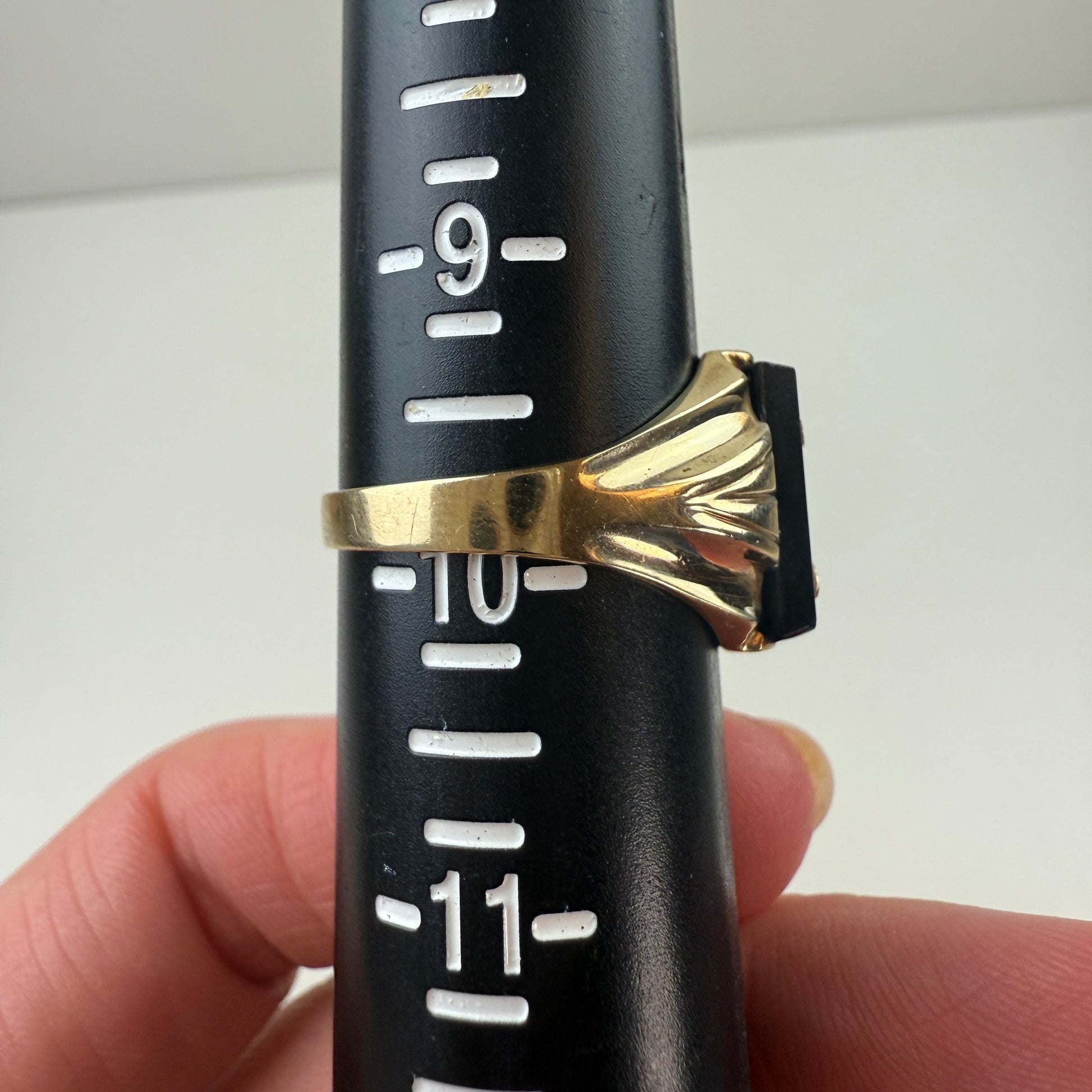 Black measuring tool with gold ring held by a hand against a white background