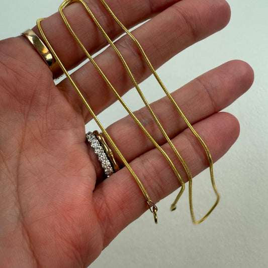 Gold 14K snake chain held in a hand with a plain background