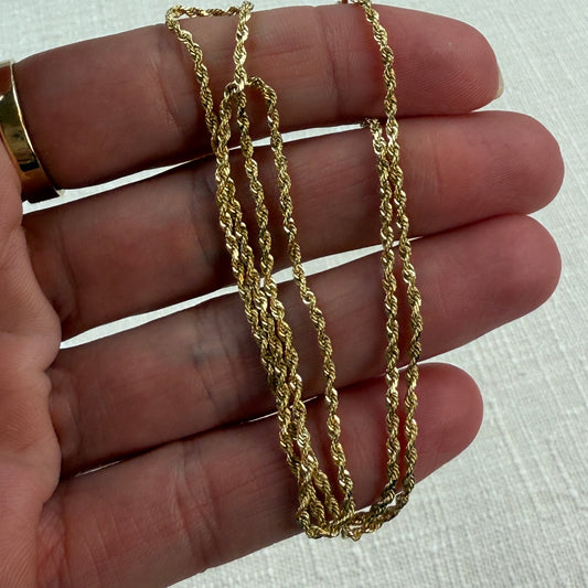 Gold chain held between fingers on a light background