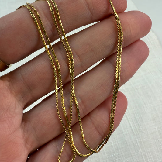 18k S-link gold chain held in a hand against a white background