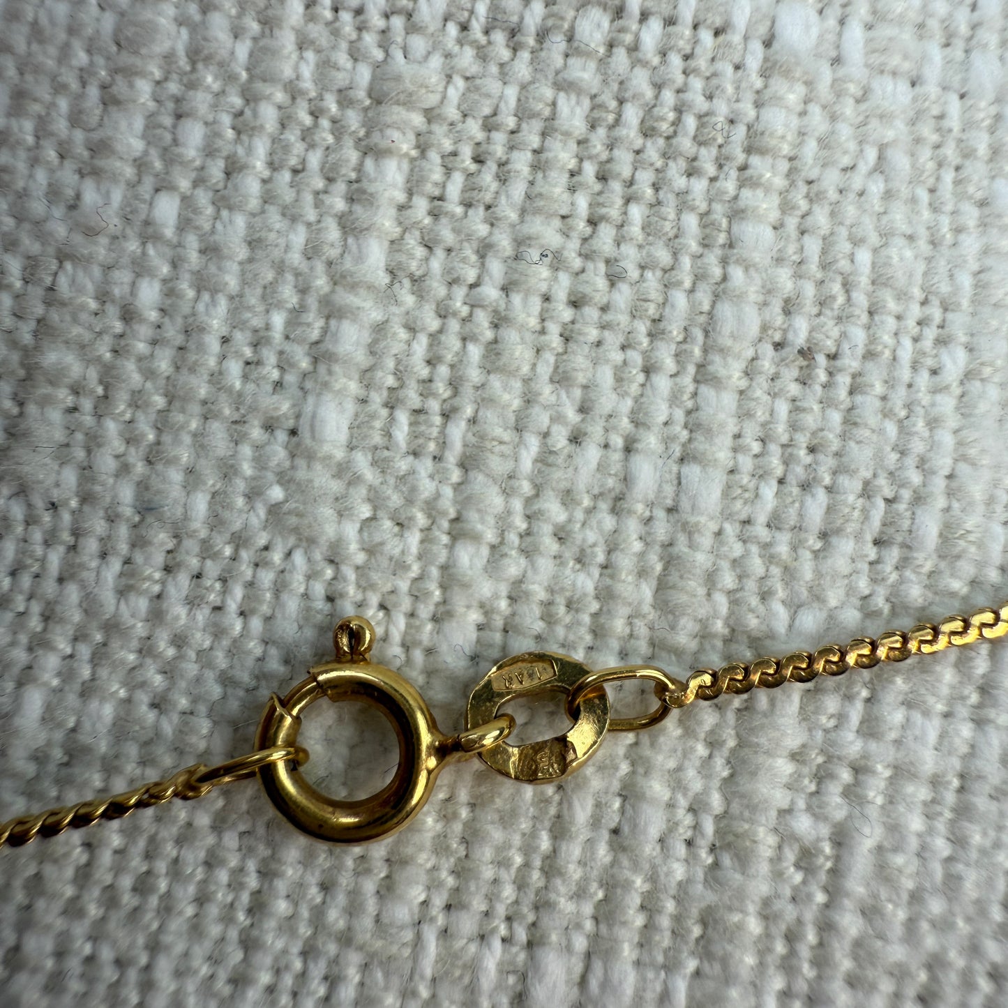 Gold necklace with spring clasp with  hallmarks on a textured beige surface