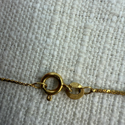 Gold necklace with spring clasp with 750 hallmark on a textured beige surface