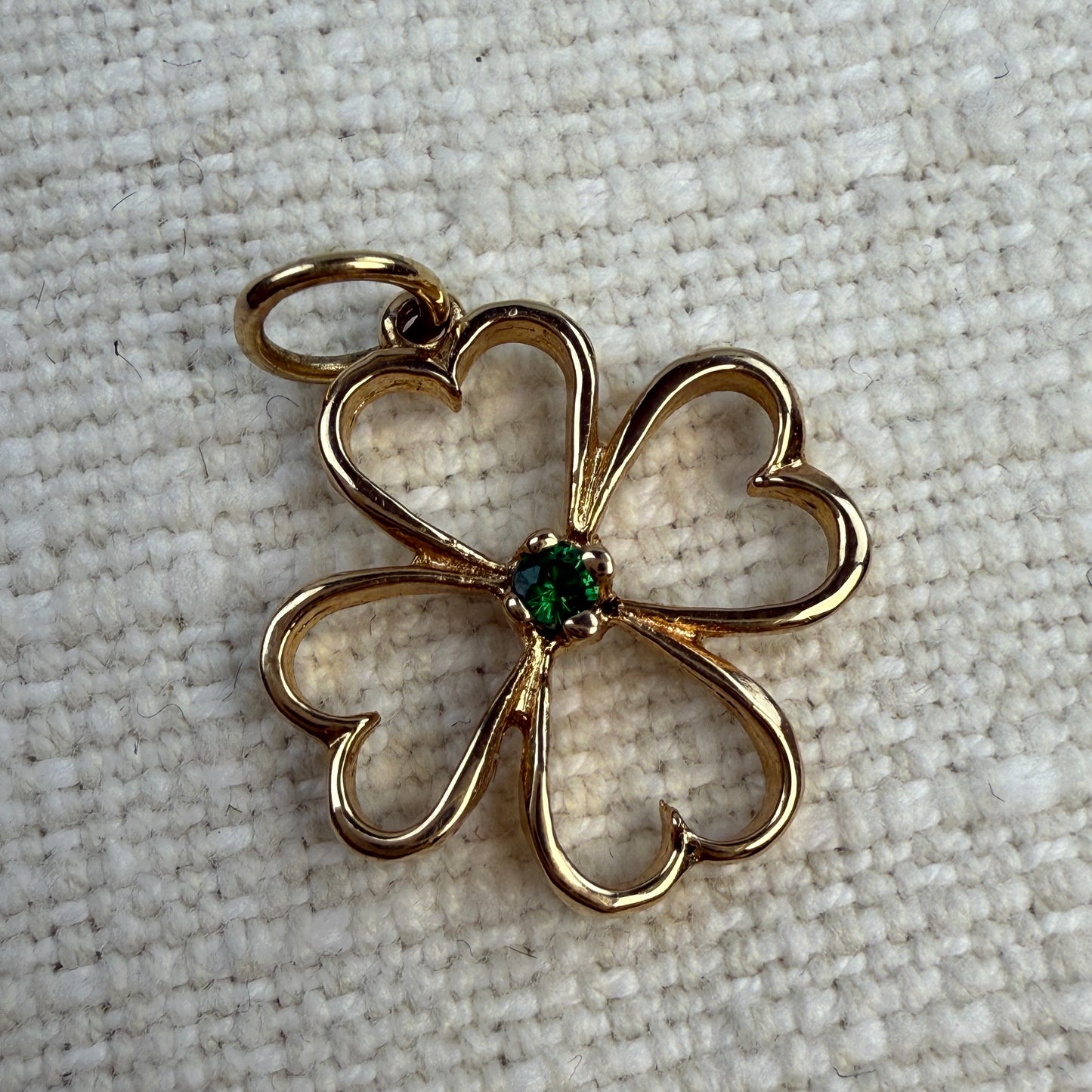 Gold four-leaf clover pendant with a green emeraldgemstone on a textured beige background