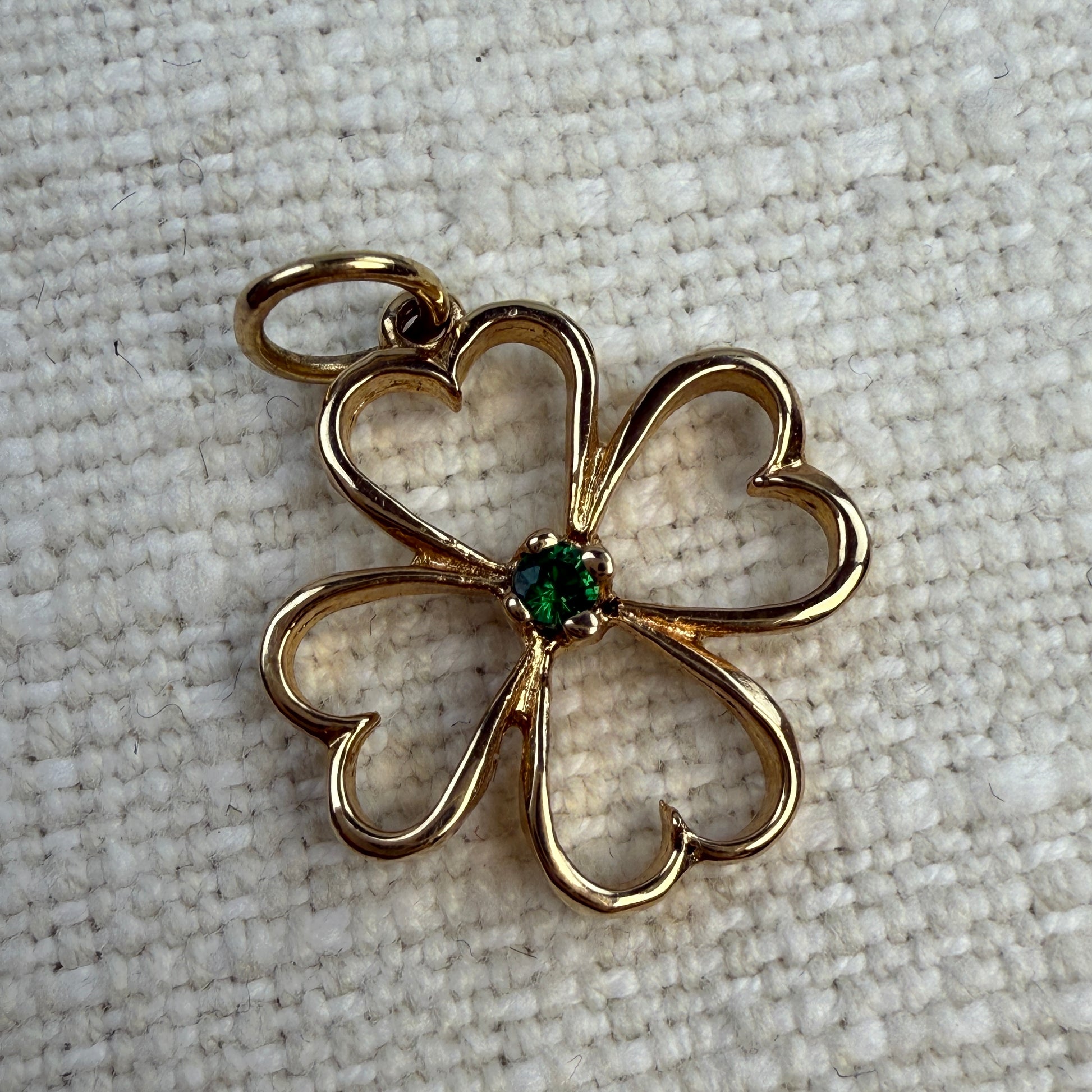 Gold four-leaf clover pendant with a green emeraldgemstone on a textured beige background
