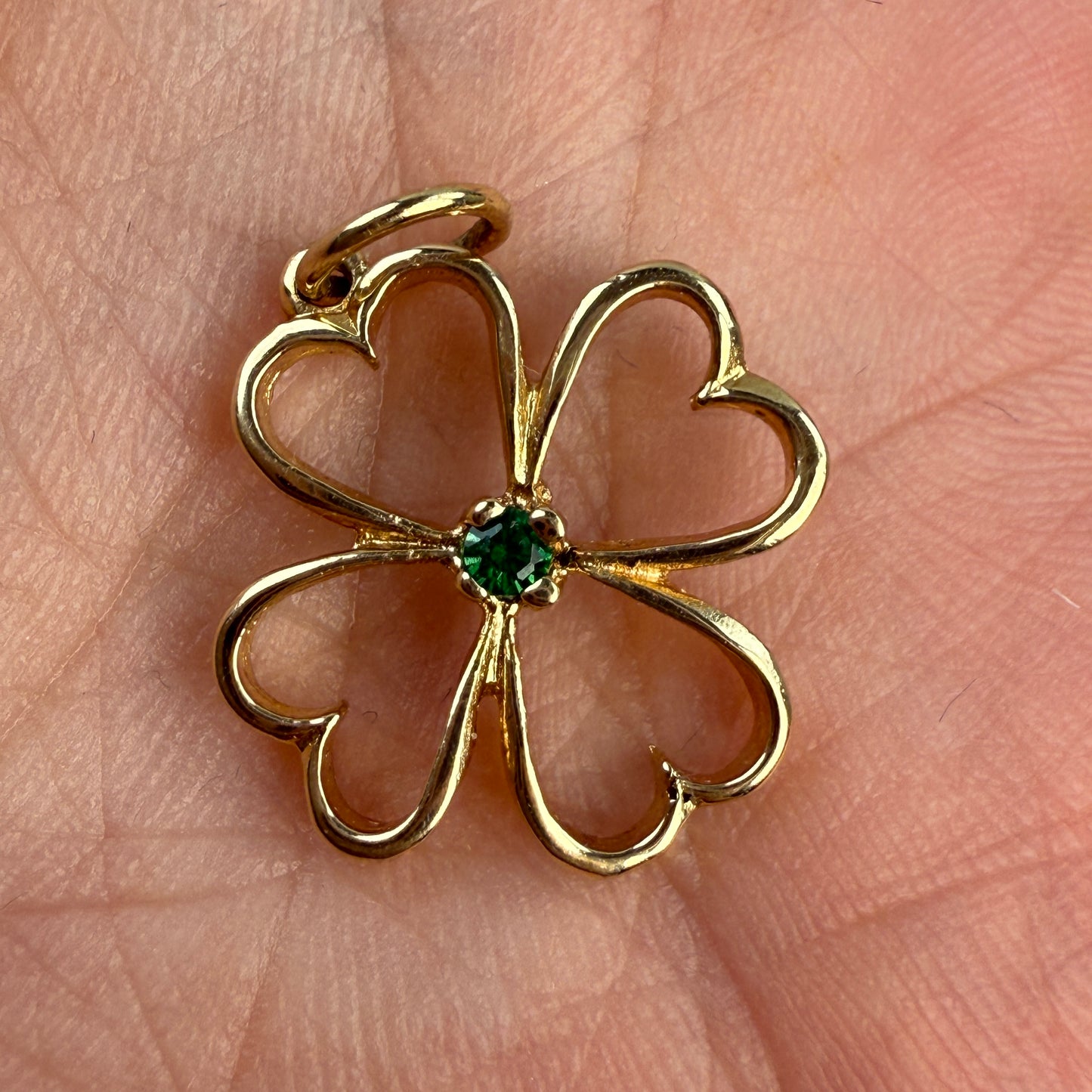 Gold four-leaf clover pendant with a green emerald gemstone on a hand.