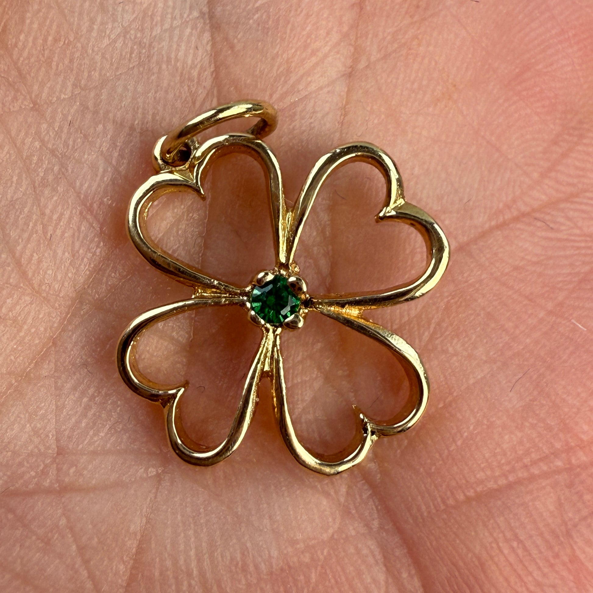 Gold four-leaf clover pendant with a green emerald gemstone on a hand.