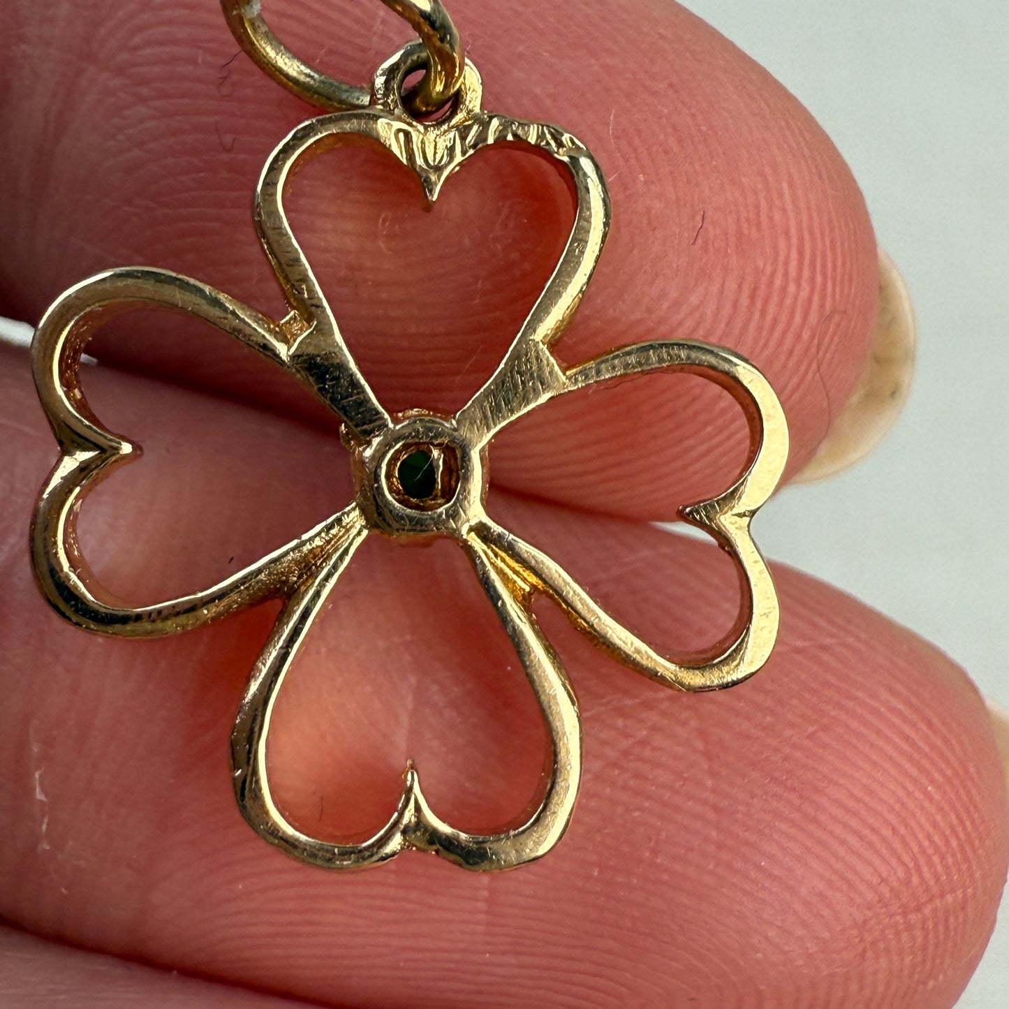 Back of the gold four-heart pendant held between fingers against a neutral background