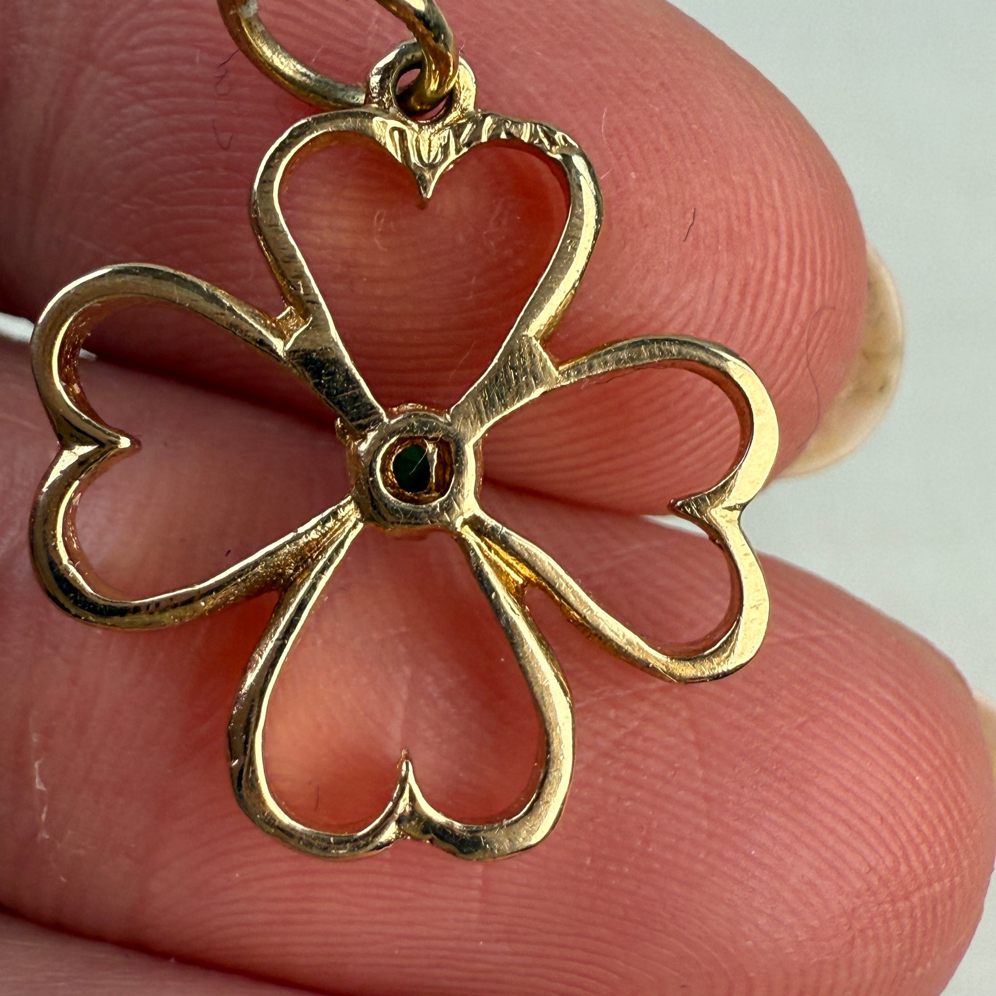 Back of the gold four-heart pendant held between fingers against a neutral background