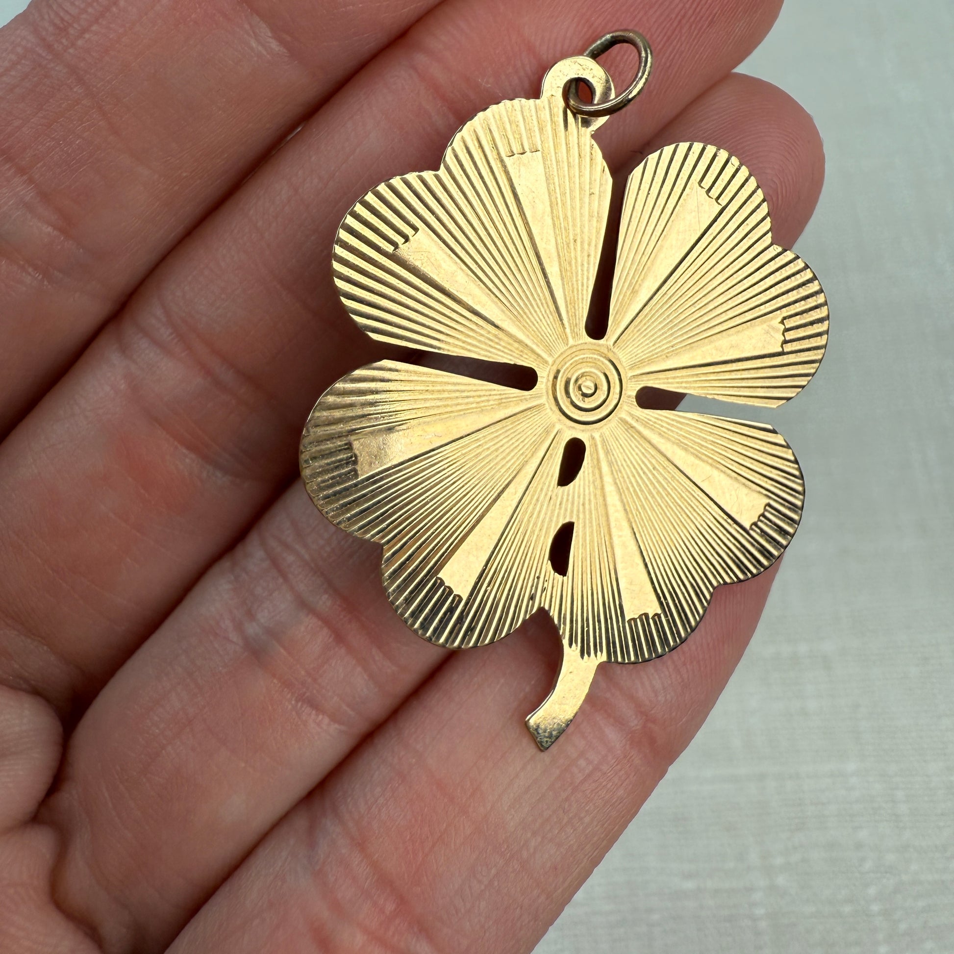 Engine turned vintage four-leaf clover pendant held in a hand with off white background