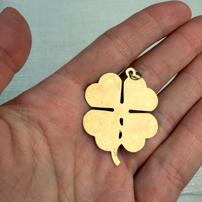 The back of an engine turned vintage four-leaf clover pendant held in a hand