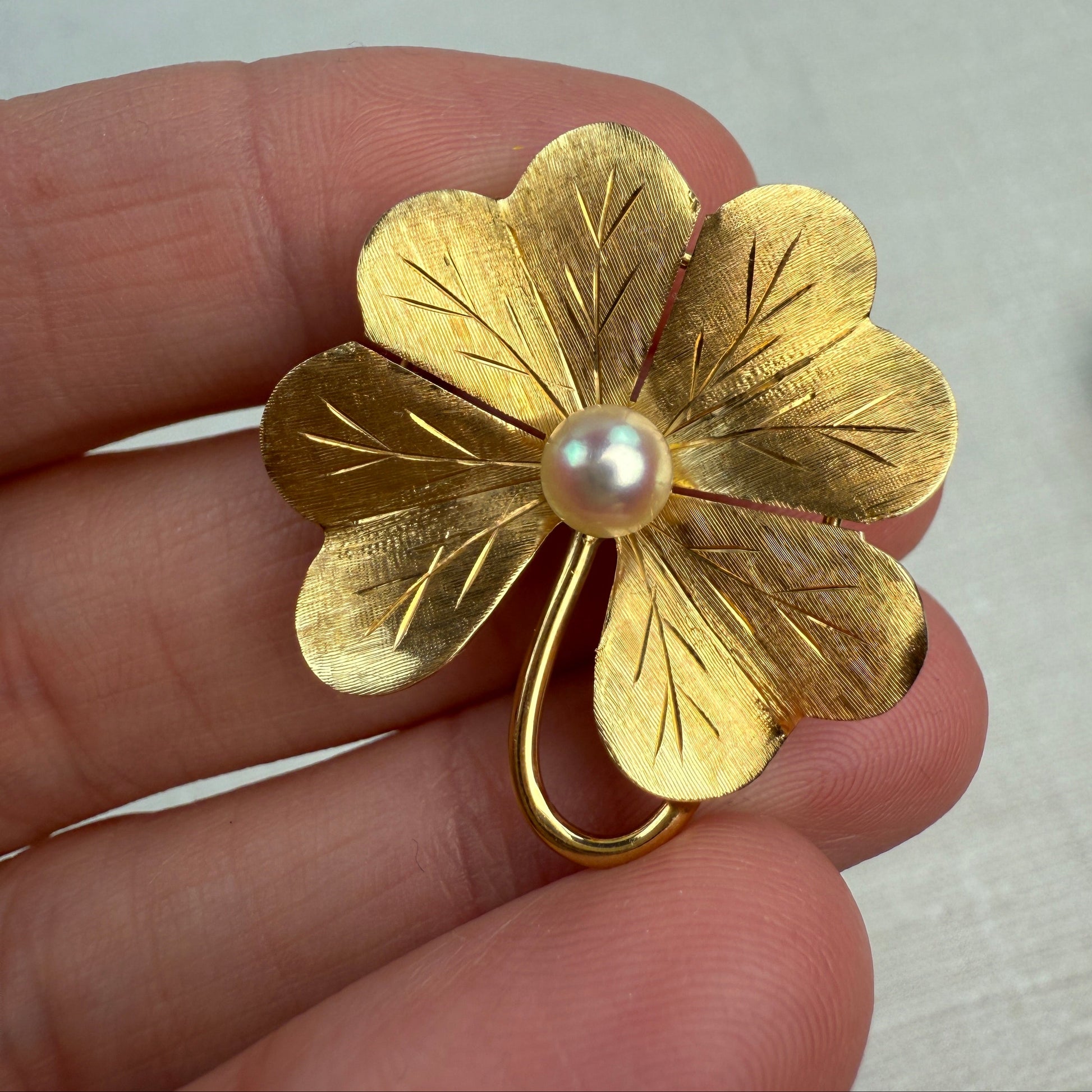 Gold four-leaf clover brooch  and pendant with a pearl held between fingers on a light background