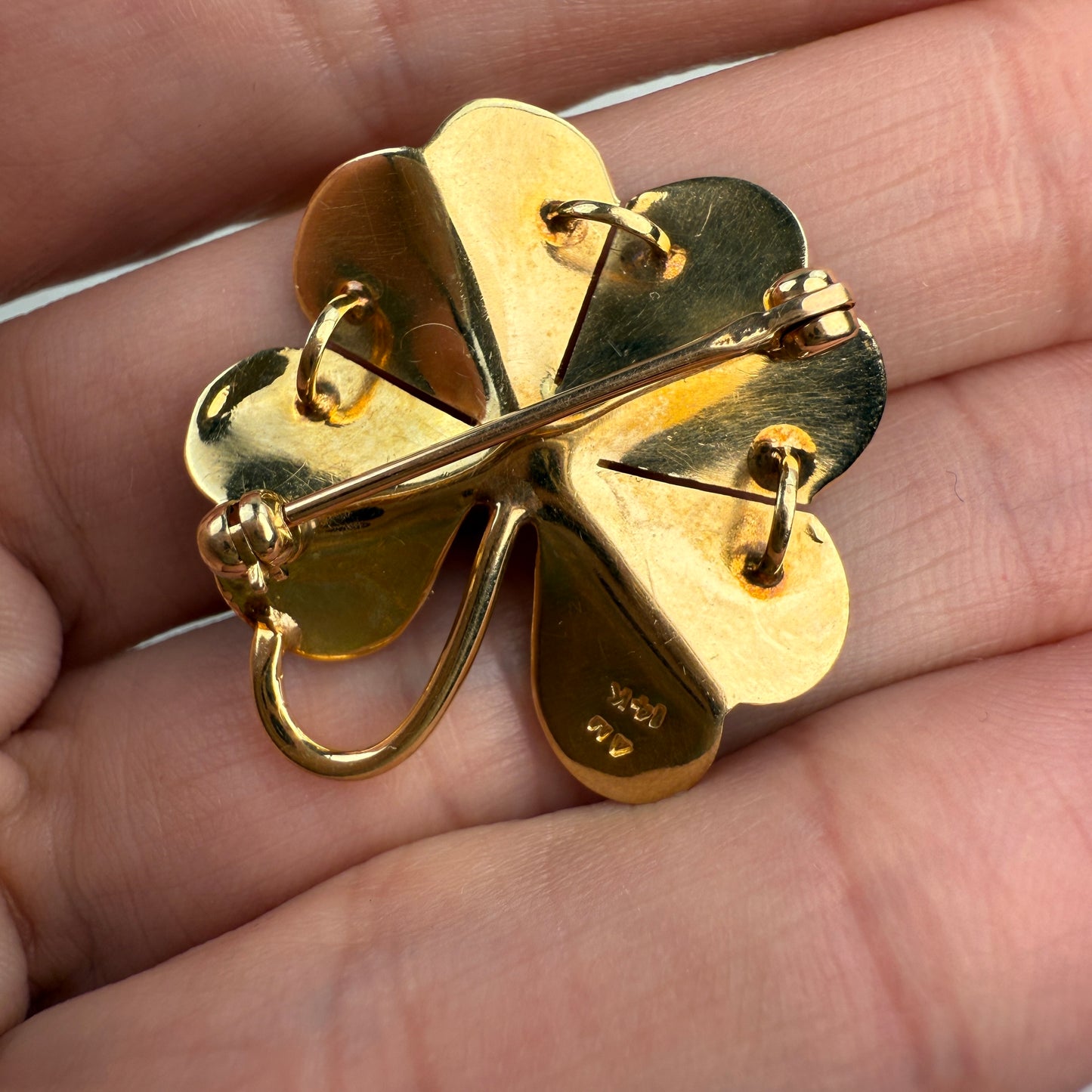 Back of the fold four-leaf clover brooch  and pendant with a pearl held between fingers on a light background
