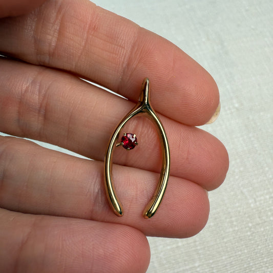 Gold wishbone-shaped pendant with a pinkish redish garnet gemstone held between fingers on a white background