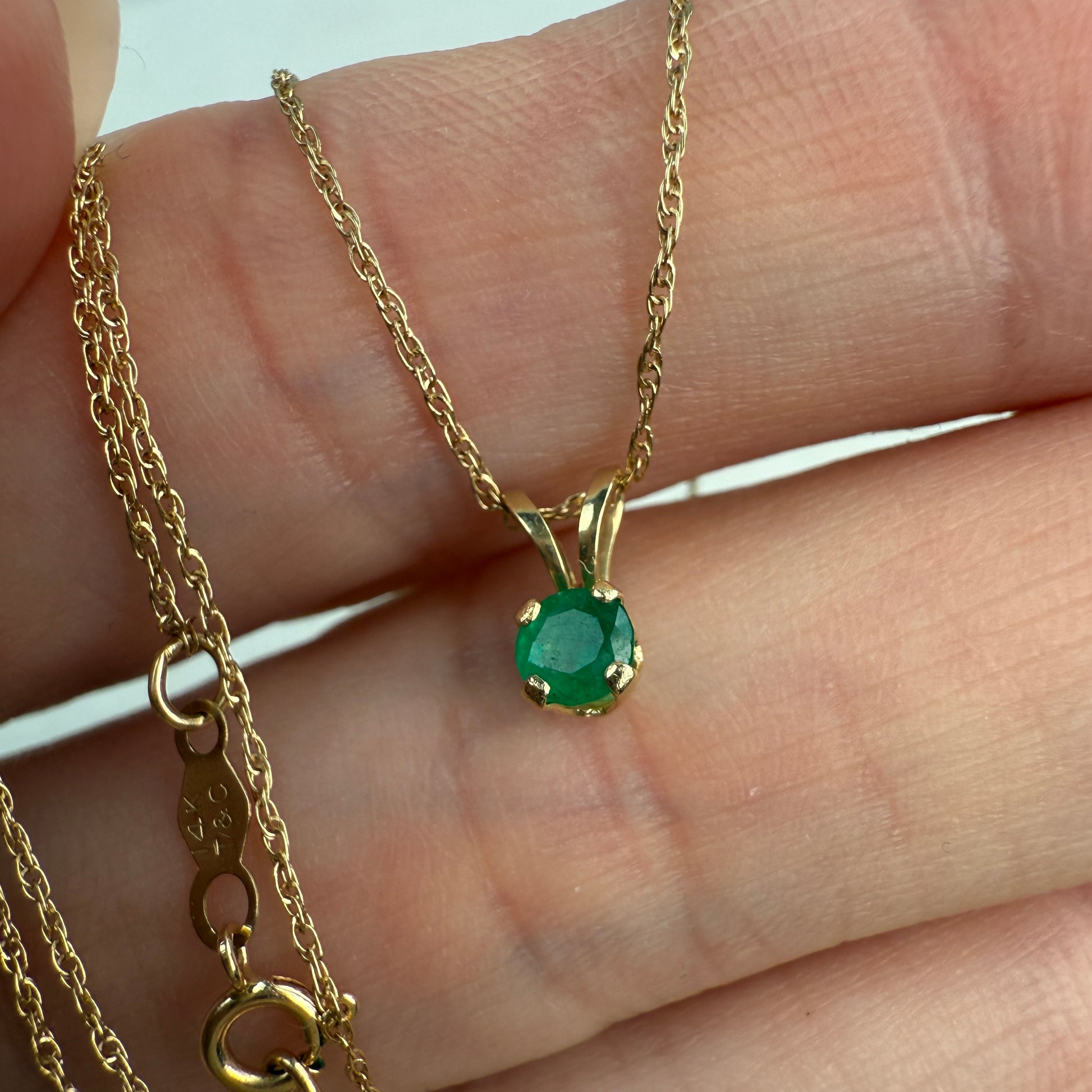 Gold necklace with a green emerald gemstone pendant held between fingers.