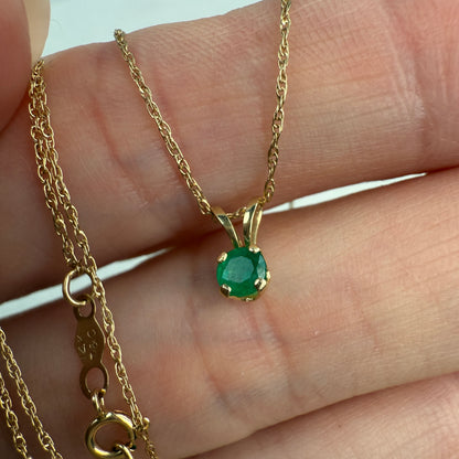 Gold necklace with a green emerald gemstone pendant held between fingers.