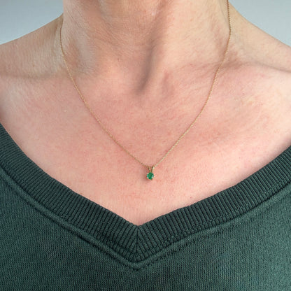 Gold necklace with a green emerald gemstone pendant worn by a person in a dark green sweater.