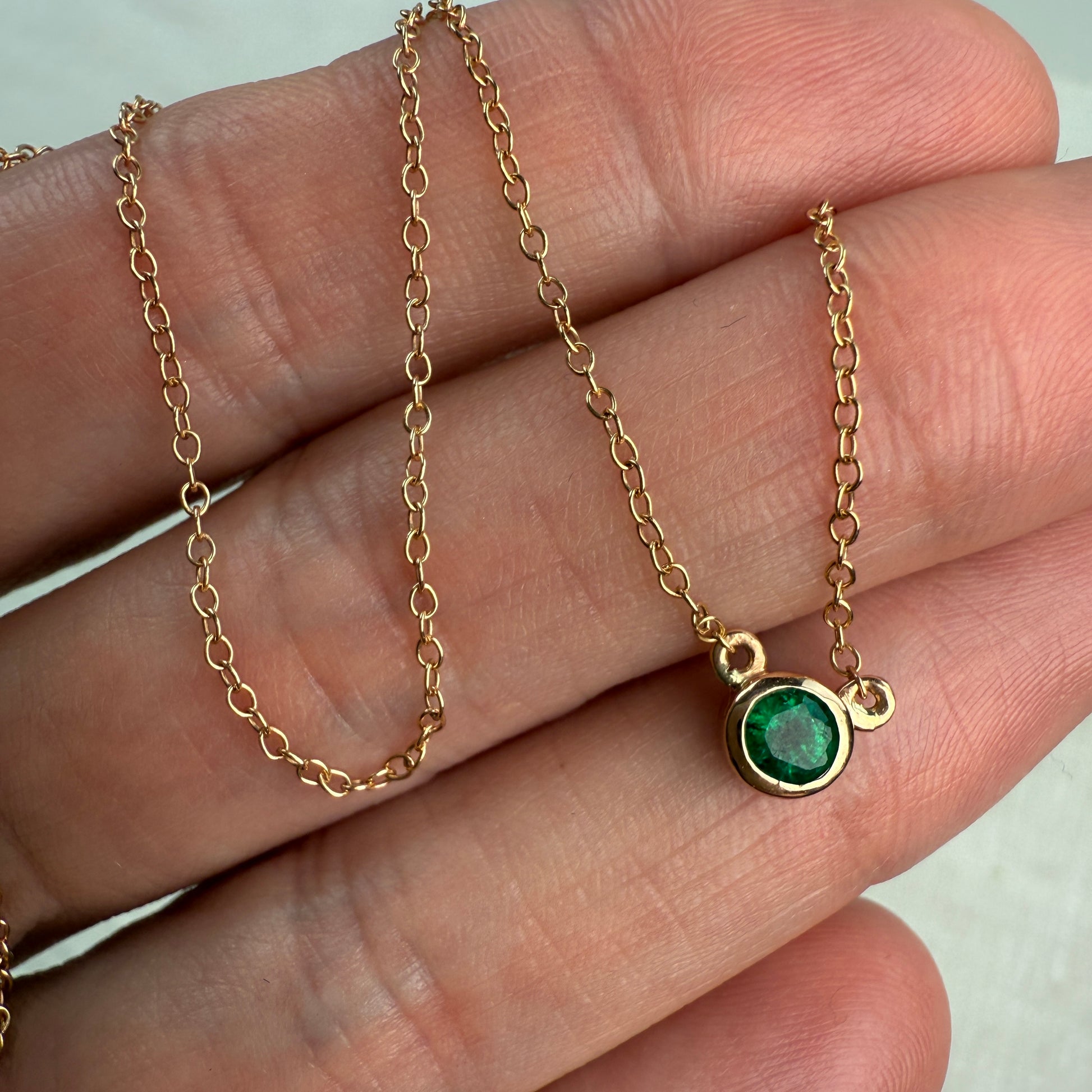 Rose gold necklace with a green emerald gemstone pendant held on a hand.