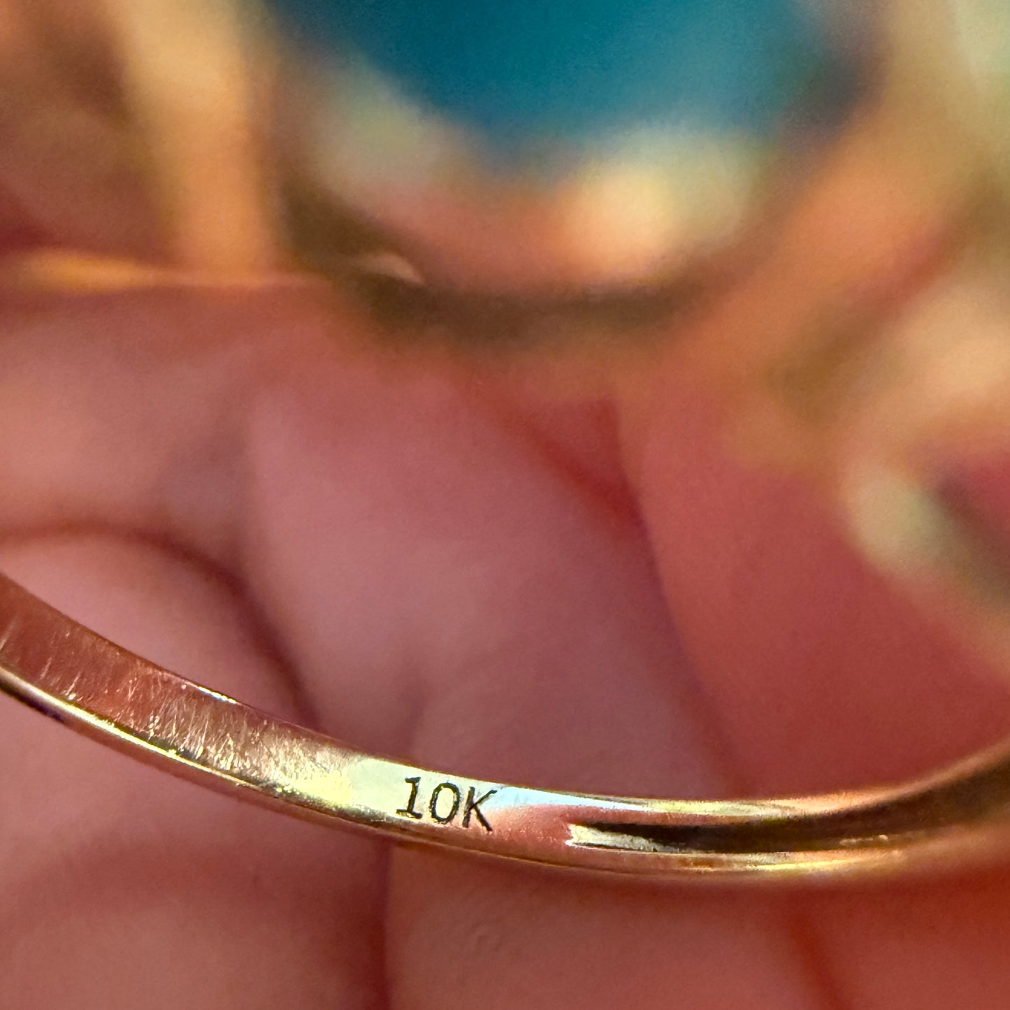 Gold turquoise ring with '10K' marking on a hand against a blurred background