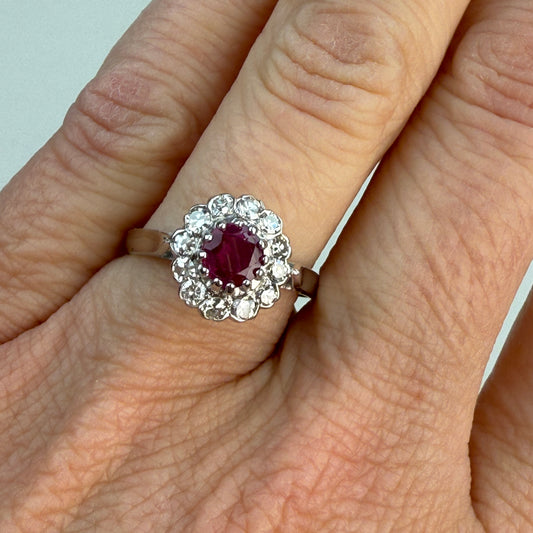 Ruby and diamond cluster ring in 18K gold on a hand with light white background. 