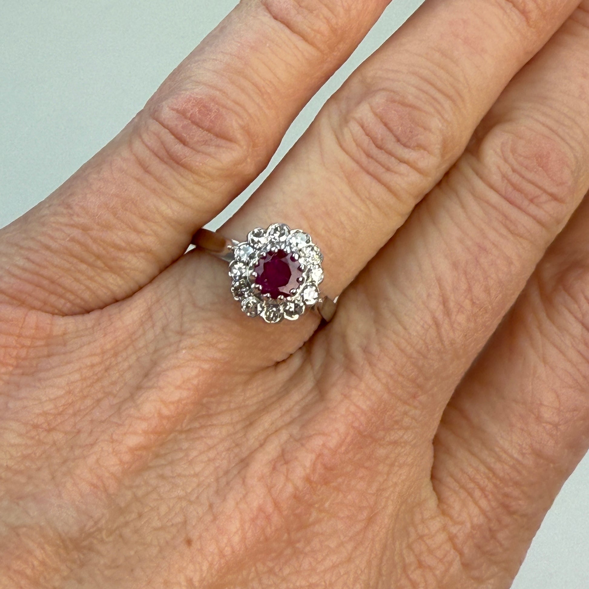 Ruby and diamond cluster ring in 18K gold on a hand with light white background. 