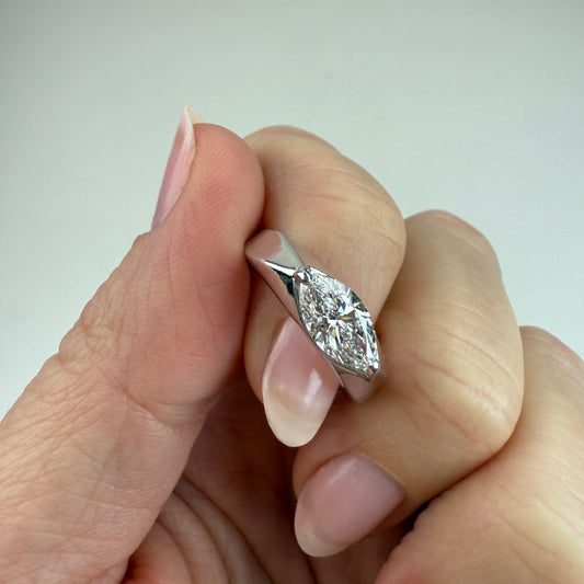White gold and 1 carat lab marquise diamond between two fingers at and angle with off-white background