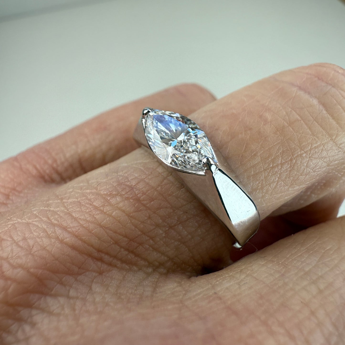 White gold ring with a 1-carat lab-grown marquise diamond on the ring finger, set against an off-white background. 