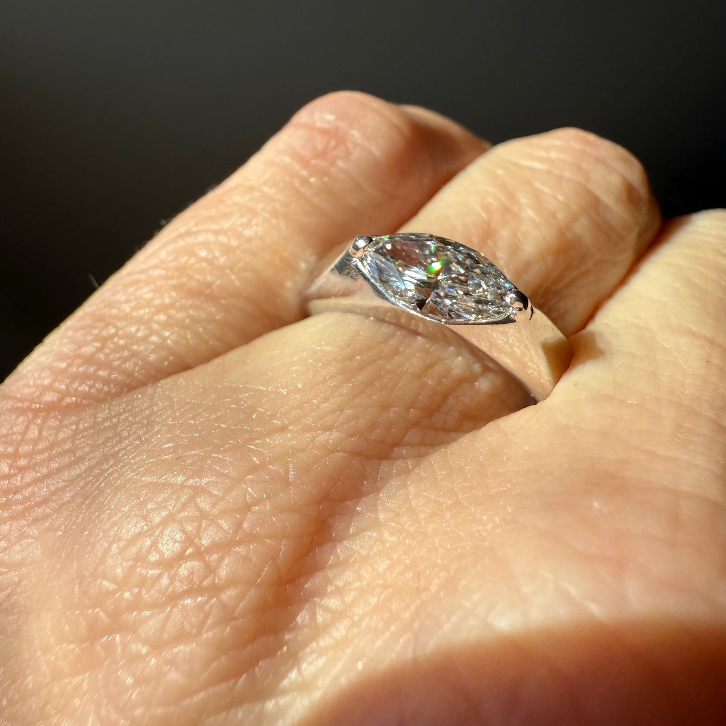 White gold and a 1-carat lab marquise diamond on the ring finger with an off-white background in the sunlight. 