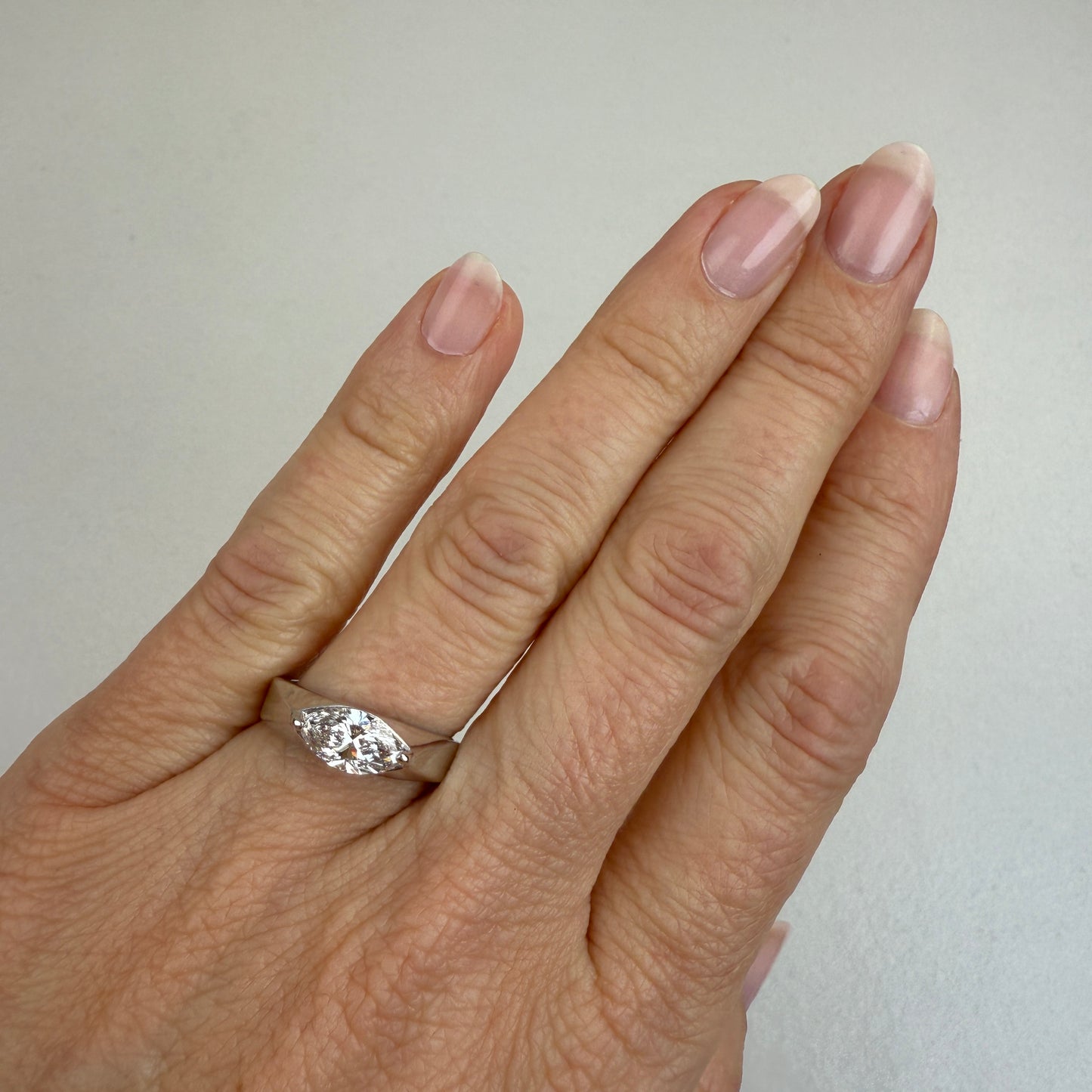 White gold and a 1-carat lab marquise diamond on the ring finger with an off-white background.