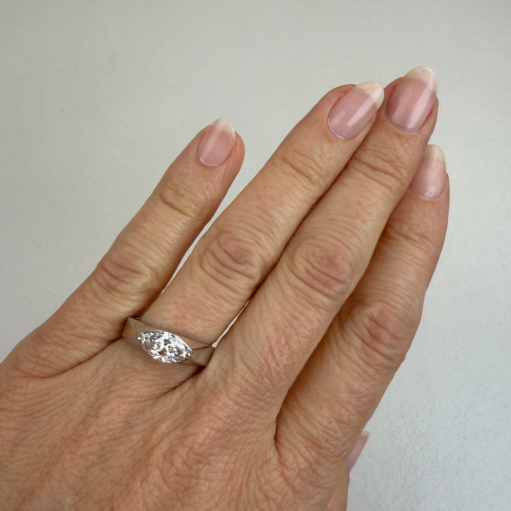 White gold and a 1-carat lab marquise diamond on the ring finger with an off-white background.