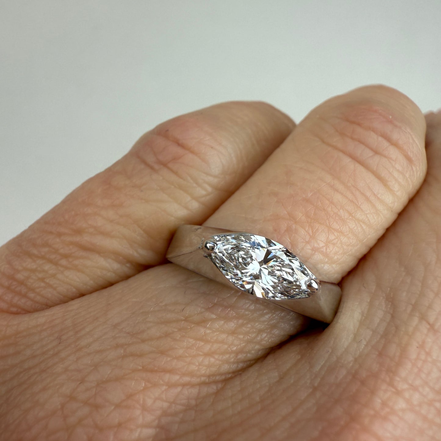 White gold and a 1-carat lab marquise diamond on the ring finger with an off-white background in the sunlight. 