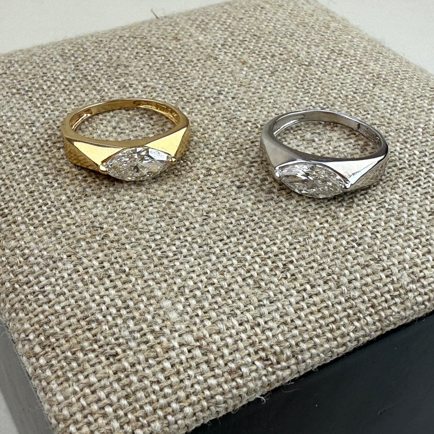 White gold and yellow gold rings with a 1-carat lab marquise diamond ring on a textured surface together