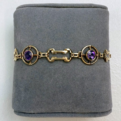 Gold bracelet with purple gemstones on a gray cushion
