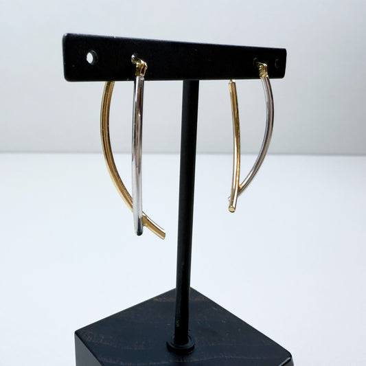 Gold hoop earrings on a black earring stand against a white background
