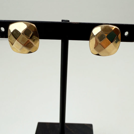 Gold earrings on a black stand against a light gray background