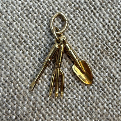 Gold-colored gardening tool charm on a textured fabric background