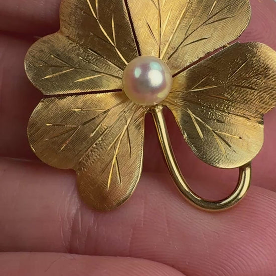 Video of the gold textured four leaf clover and pearl in hand moving slowly. 