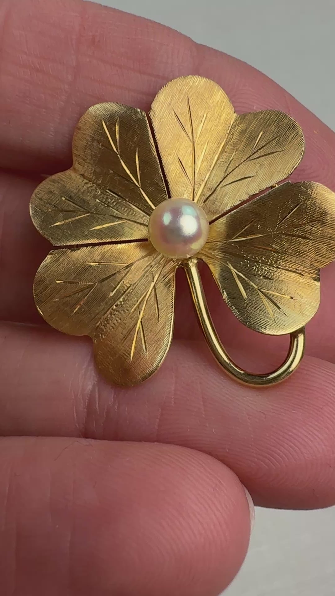 Video of the gold textured four leaf clover and pearl in hand moving slowly. 