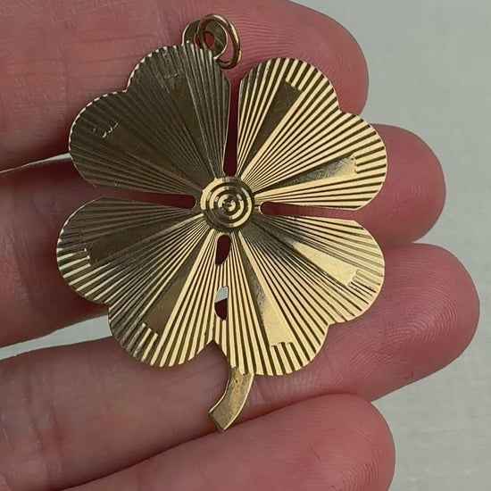 Video of an engine turned vintage four-leaf clover pendant held in a hand and slowly moving. 