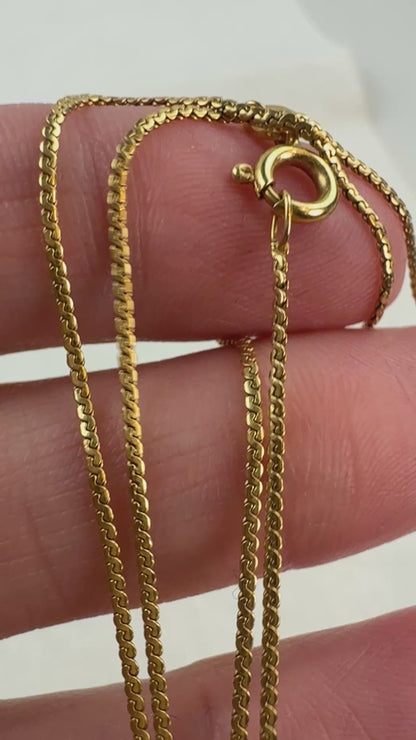 Video of yellow 18K yellow gold s-link chain moving in a hand with an off white background