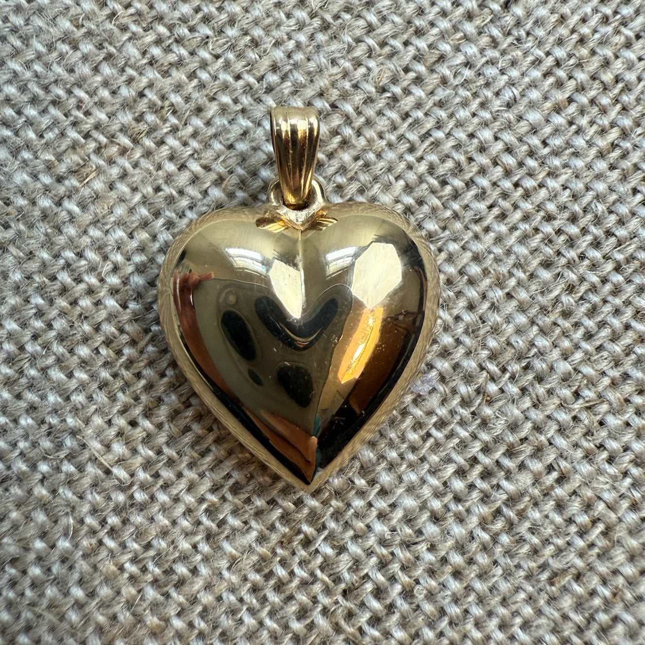 Gold heart-shaped pendant on a textured beige fabric background