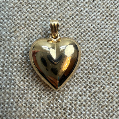 Gold heart-shaped pendant on a textured beige fabric background