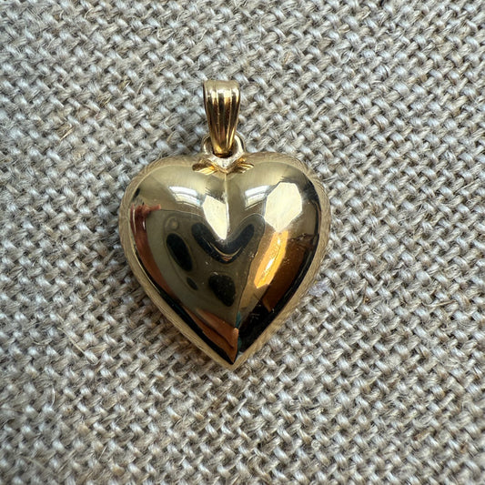 Gold heart-shaped pendant on a textured beige fabric background