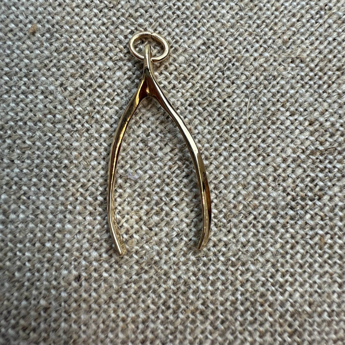 Gold wishbone pendant on a textured beige fabric background